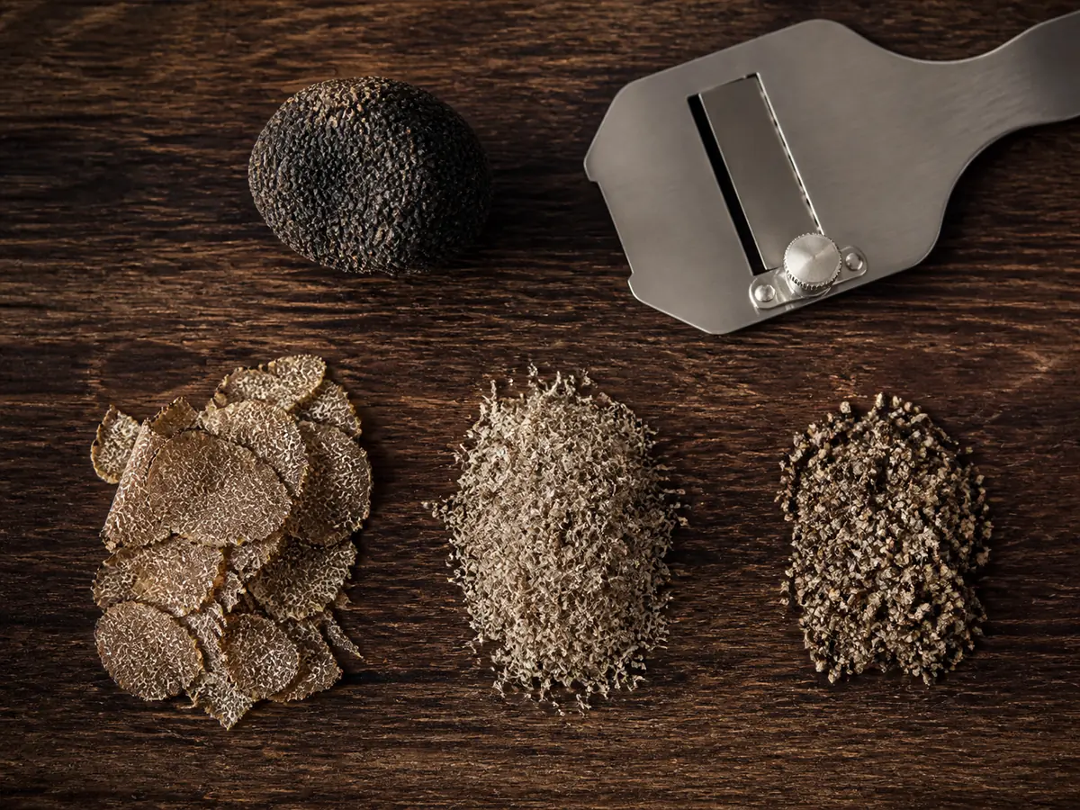 Fresh black truffle shown as paper-thin shavings, fine grating, and a small even mince beside the intact ingredient