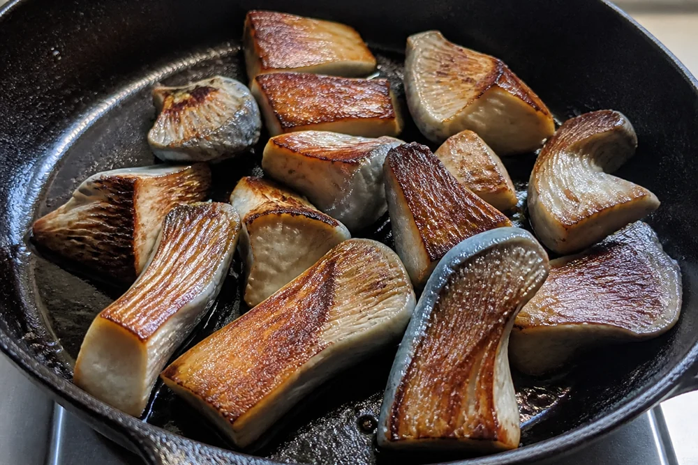 Thick pieces of blue oyster mushroom searing in a cast iron pan with deep brown crust forming on the cut faces