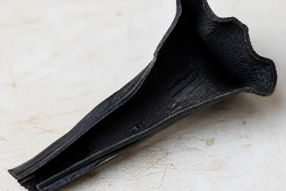 A single black trumpet mushroom split open lengthwise on a pale board showing the hollow funnel and how thin the wall is