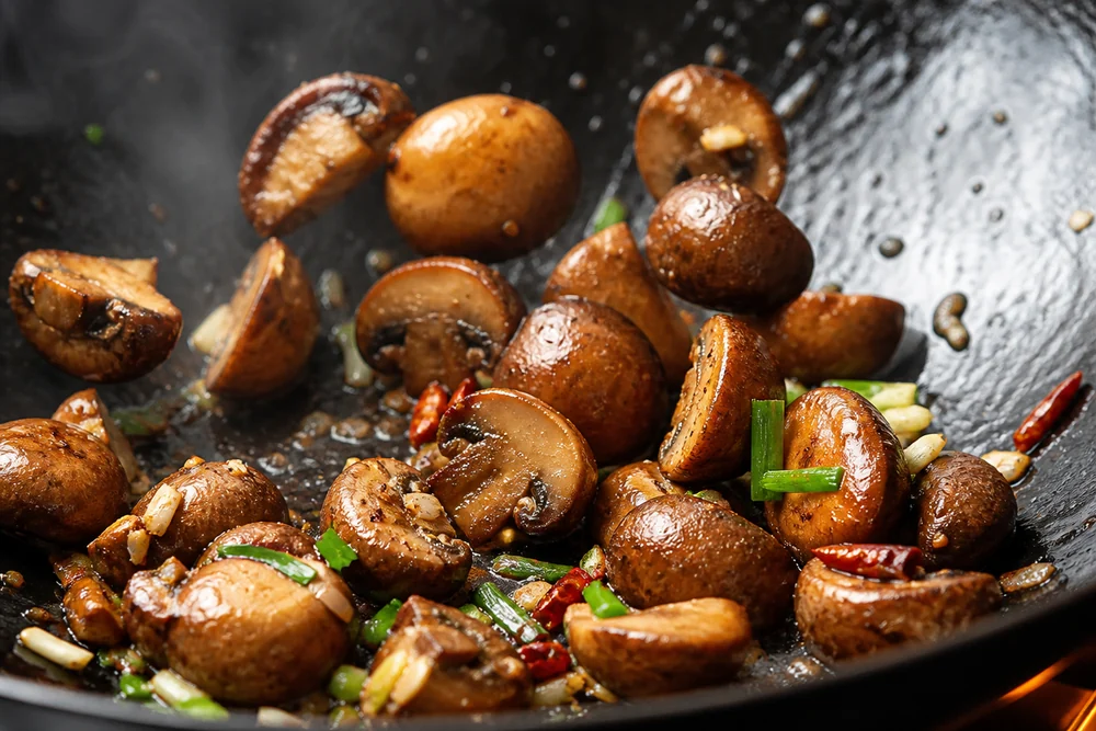Chestnut mushrooms stir-frying over high heat in a wok, browned and still visibly firm and separate
