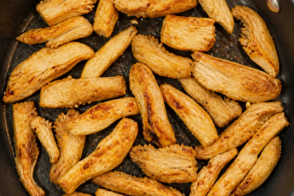 Strips of chicken of the woods cooking thoroughly in a covered skillet, fully opaque and lightly browned with no translucency left
