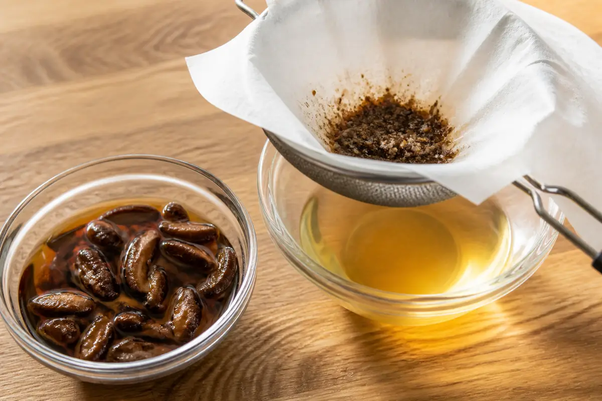 Rehydrated dried porcini beside a fine strainer and a bowl of clear amber soaking liquid