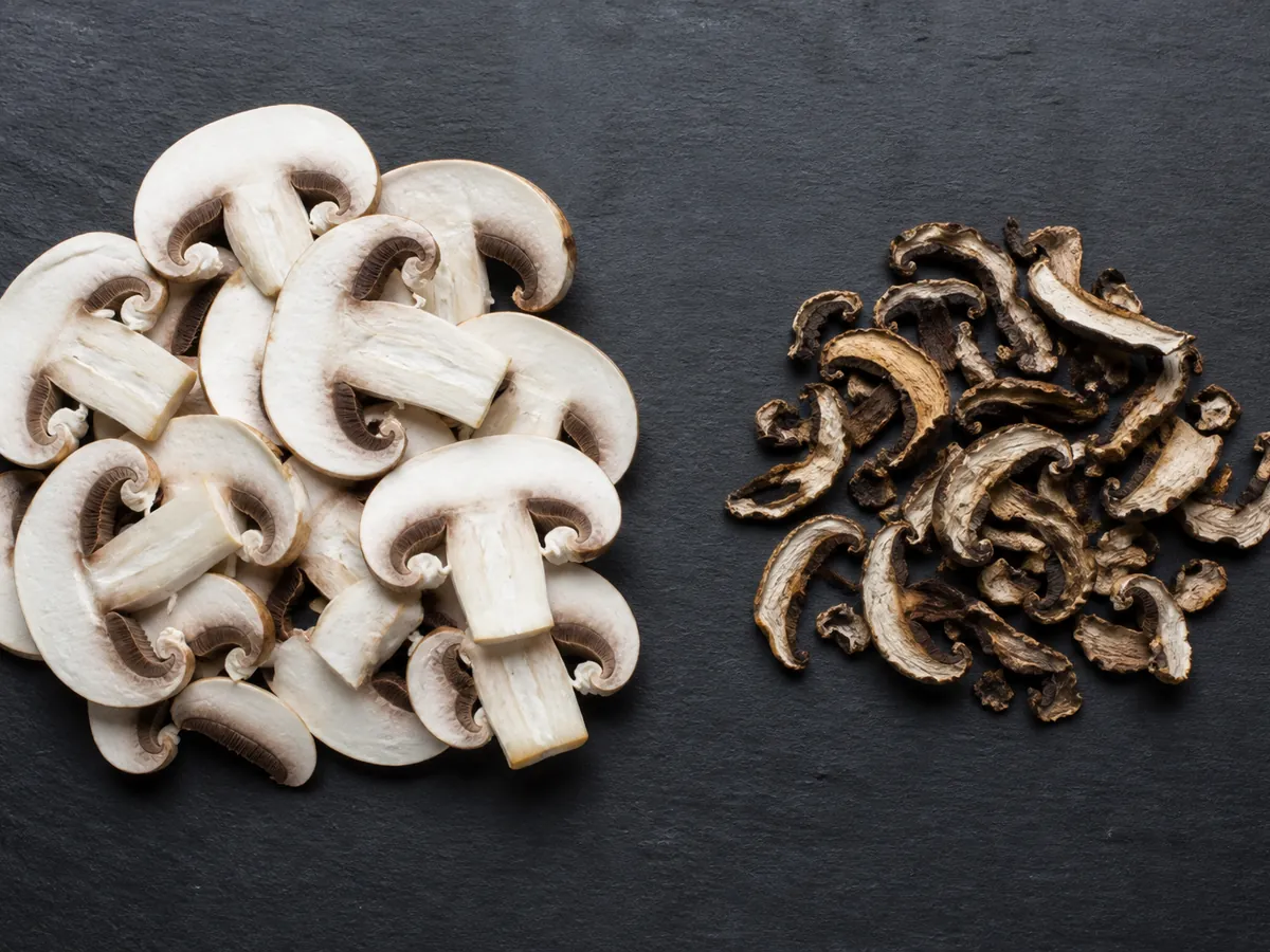 Pile of fresh mushroom slices beside the same number of slices after drying, shrunken and dark