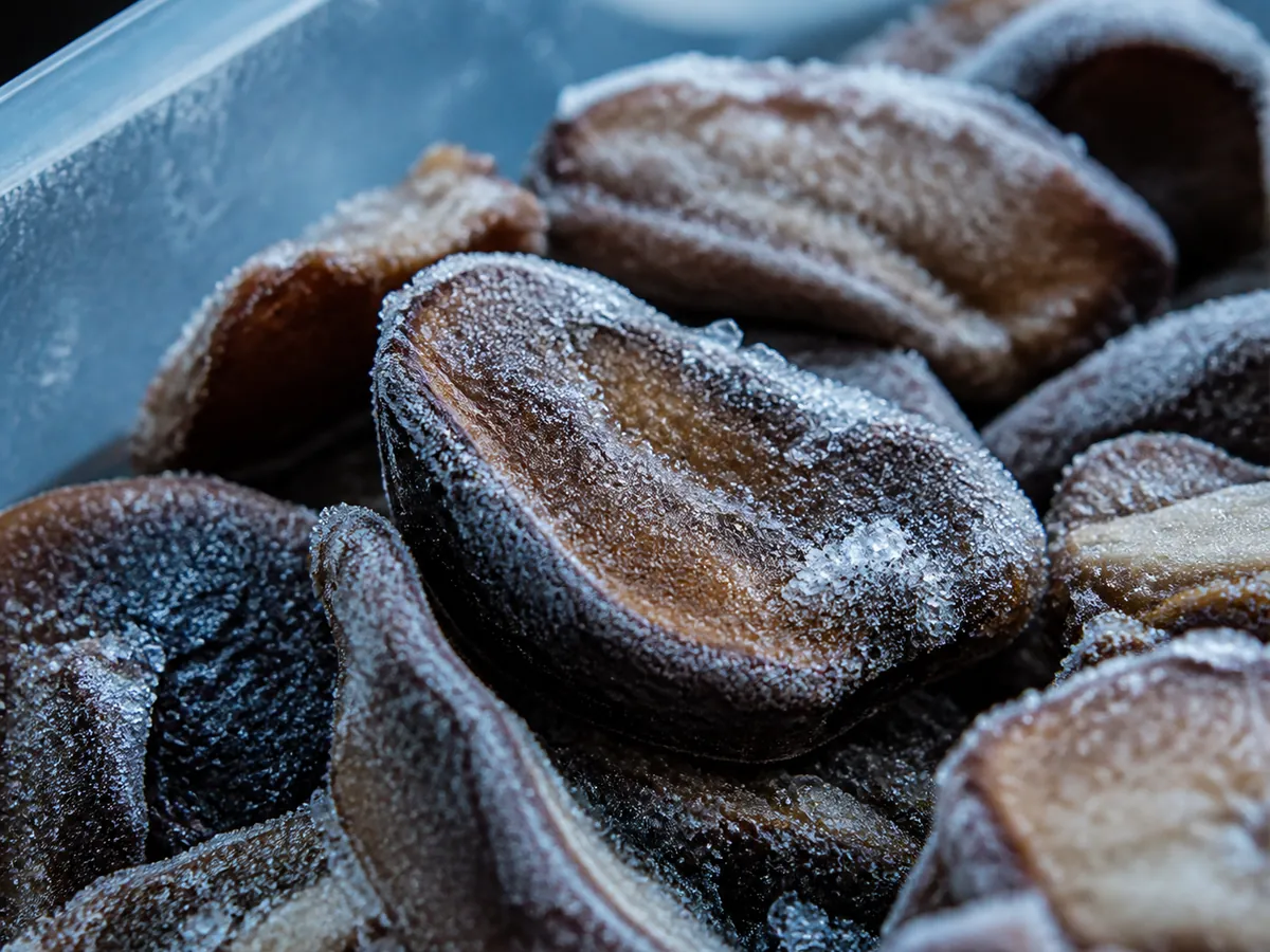 Extreme close-up of frozen mushroom pieces with fine white ice crystals on their surfaces
