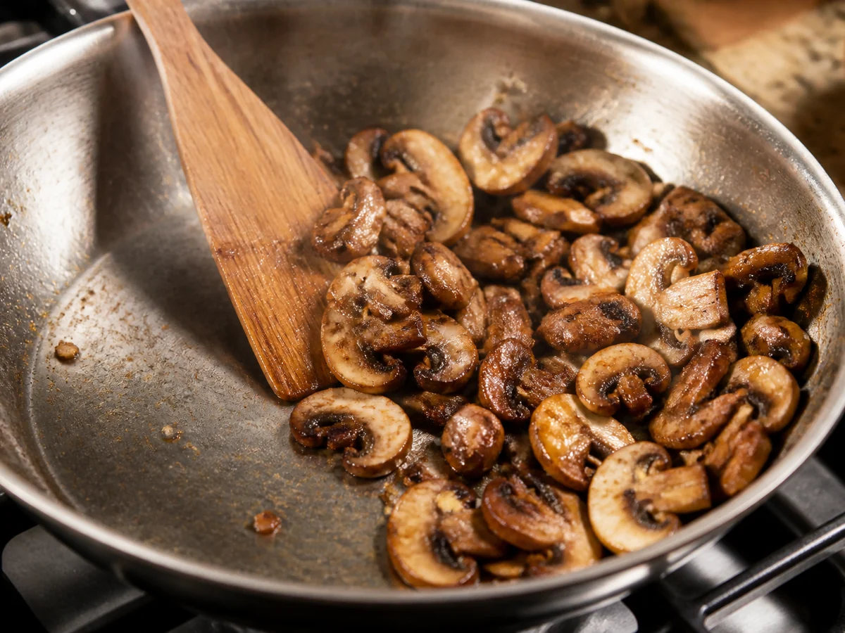 Sliced mushrooms browning in a wide frying pan with the juices reduced almost away