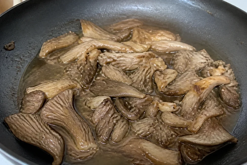 Overcooked golden oyster mushrooms collapsed and gray-brown in a pan, limp and sitting in released liquid