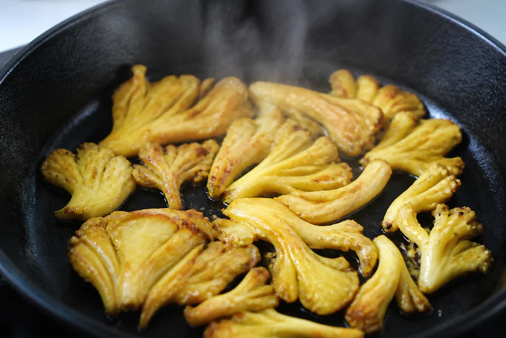 Golden oyster mushroom clusters searing in a hot dry skillet with the edges just turning brown while the centres are still yellow