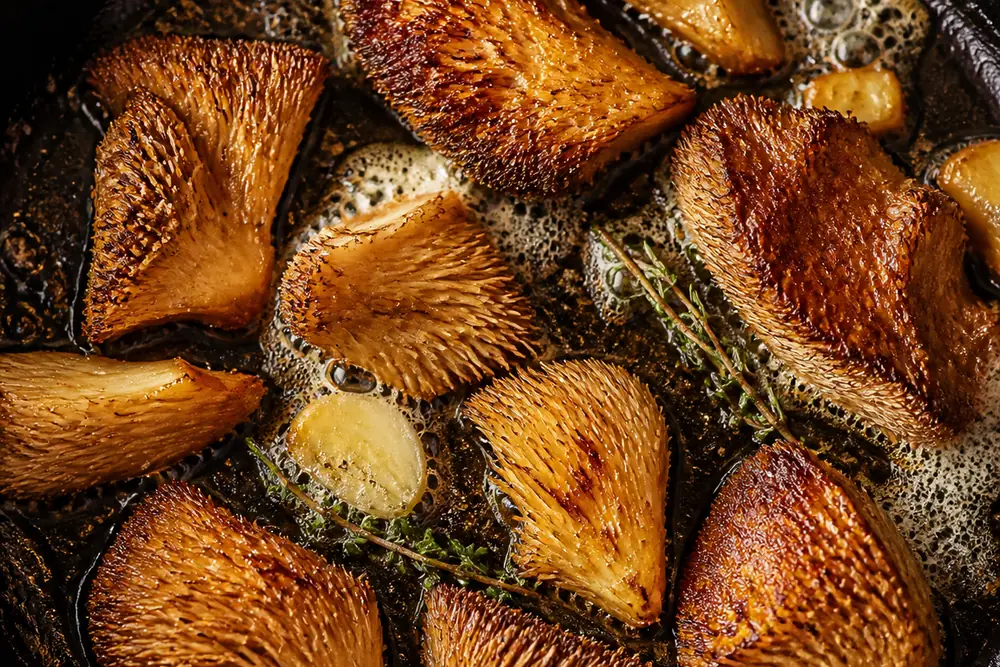 Hedgehog mushrooms searing in a cast iron pan with butter, firm and deeply browned