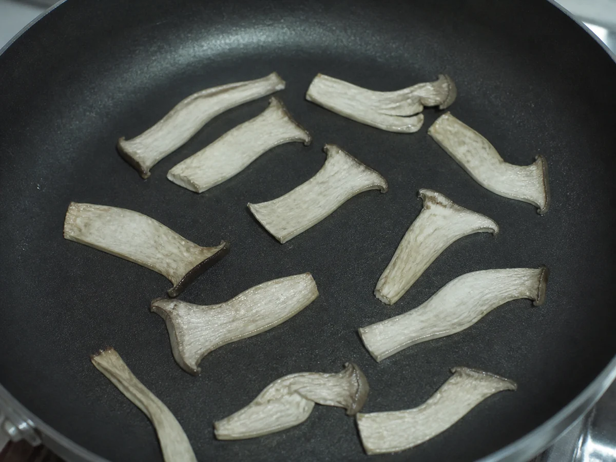 Thin king oyster slices in a pan looking pale, shrunken and leathery with no browning