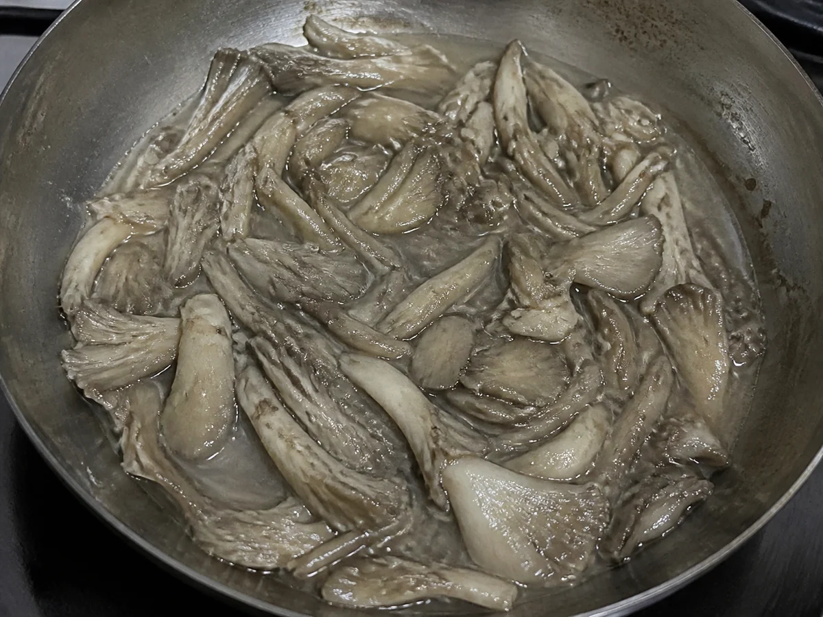 Oyster mushroom pieces collapsed in a lukewarm pan, limp and gray and sitting in released liquid with no browning