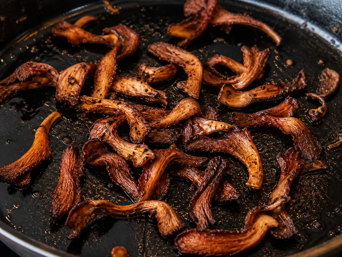 Thin pink oyster mushroom strips cooked hard in a cast iron pan until dark brown and crisp at the edges, curled and shrunken