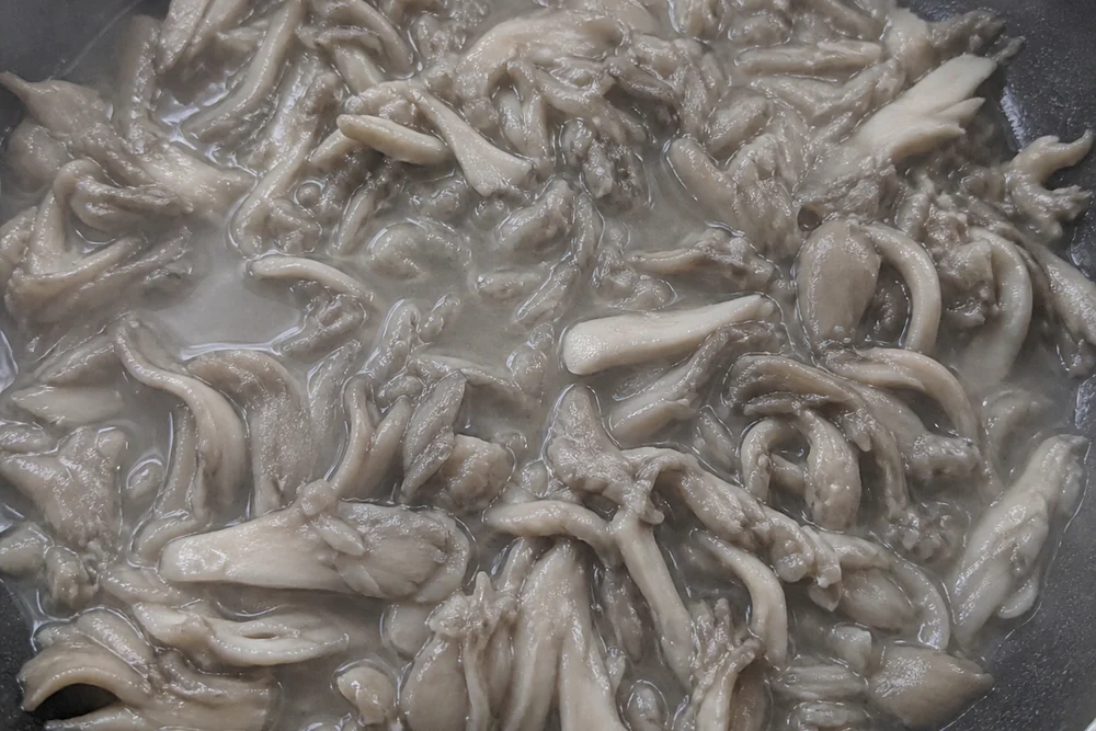 Maitake mushroom pieces steaming gray and limp in a crowded pan sitting in released liquid with no browning at all