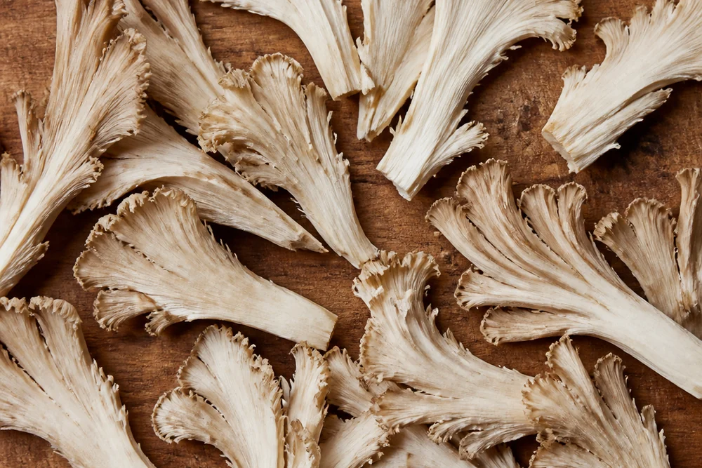 Maitake mushroom torn by hand into flat sheets along the natural frond lines, arranged on a board showing the ruffled feathered edges