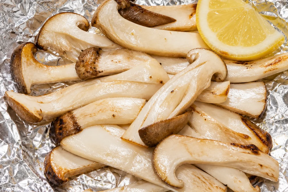 Matsutake strips with a slice of lemon on an open sheet of foil over a grill, barely cooked
