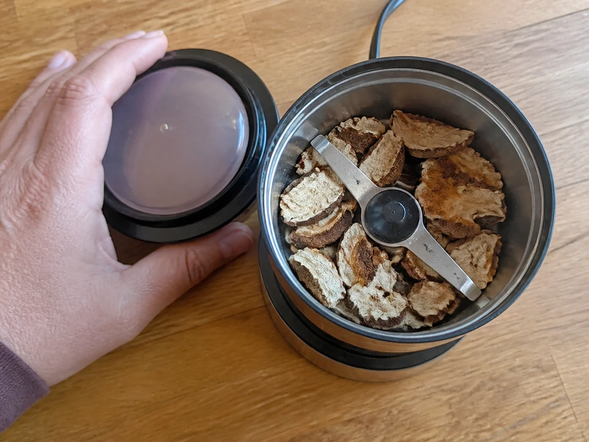 Looking down into a small electric blade grinder half filled with broken dried mushroom pieces