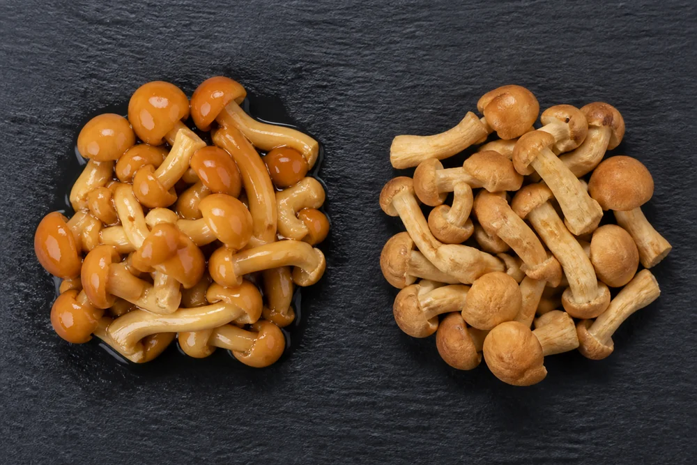 Two piles of nameko mushrooms side by side on a dark board, one glossy with the coating intact and the other dull and matte after rinsing