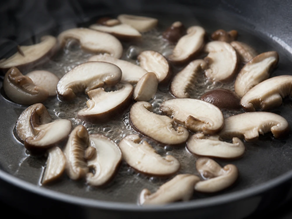Pale shiitake slices releasing moisture and steam in a skillet