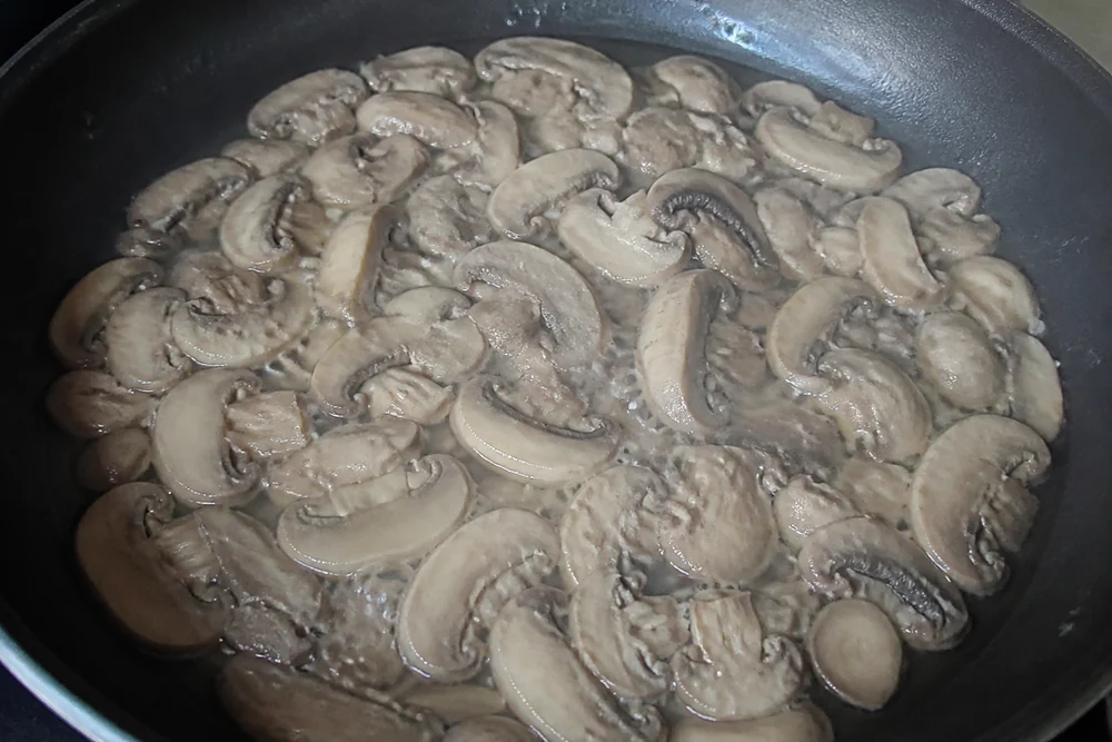 Sliced mushrooms crowded in a pan releasing water and simmering in their own gray liquid rather than browning, pale and limp