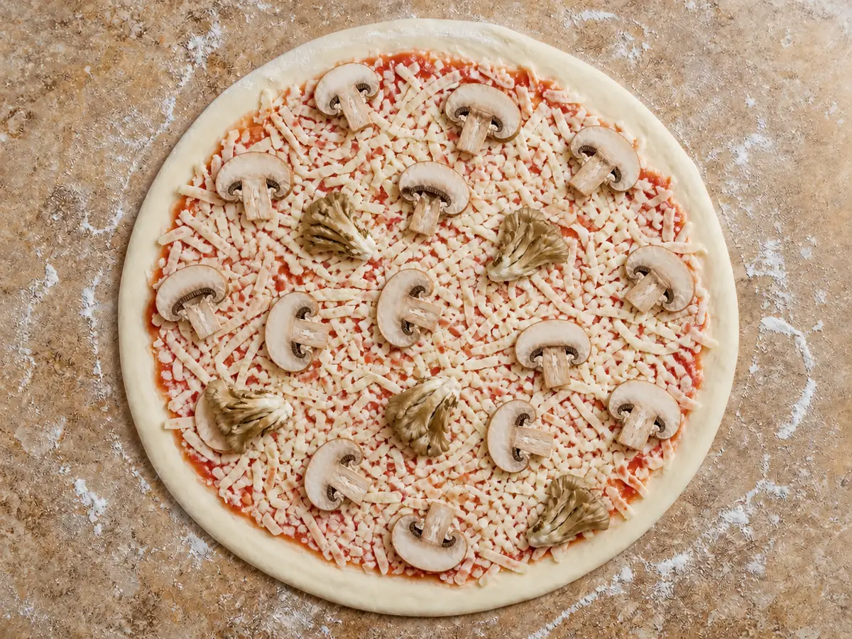 Unbaked 12-inch pizza with evenly spaced cremini slices and smaller maitake clusters