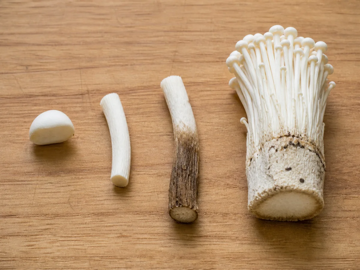 Velvet shank cap, tender upper stem, dark fibrous lower stem, and the compact base of a cultivated enoki cluster arranged on a board