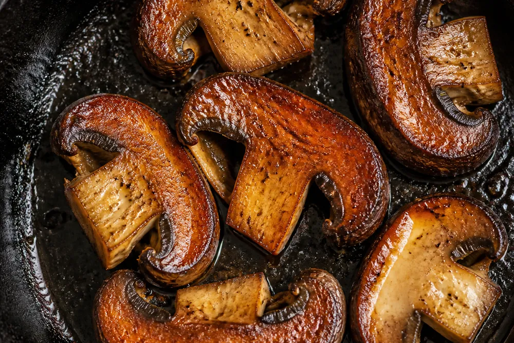 Thick slices of young wine cap mushroom searing in a cast iron pan, deeply browned on the cut faces