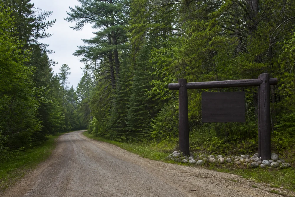 A gravel road running into a large northern Wisconsin pine and hardwood national forest with a wooden entrance marker at the roadside