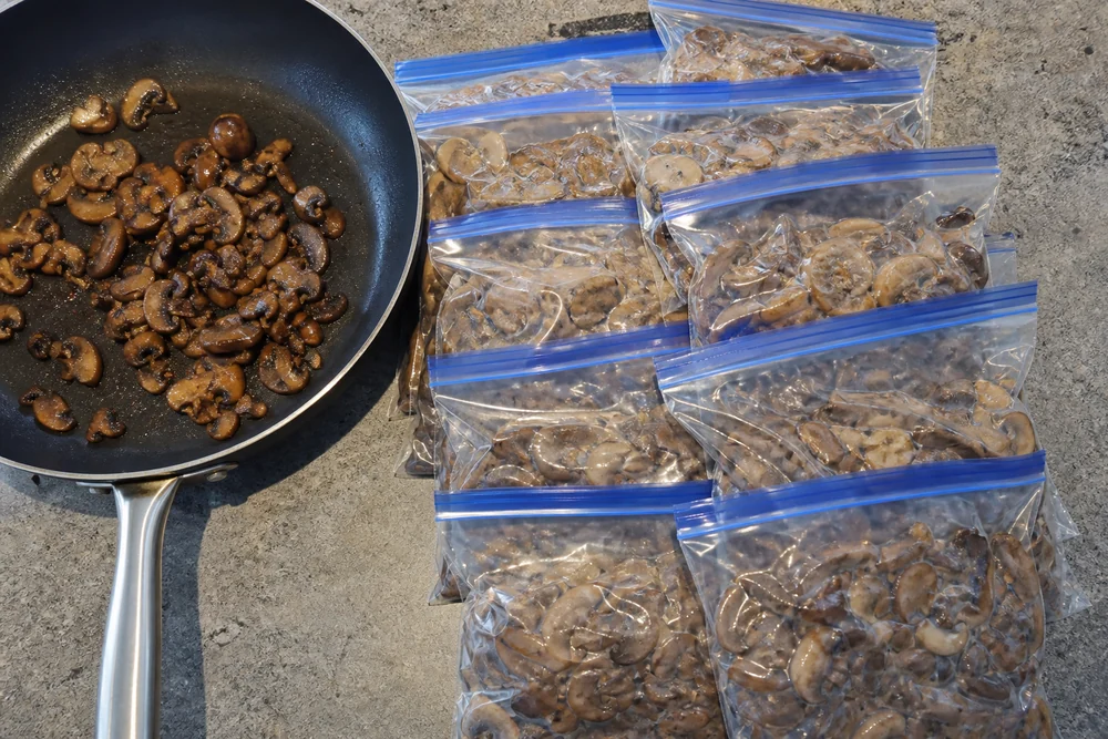 Flat labeled packets of cooked wild mushrooms stacked in an open freezer drawer