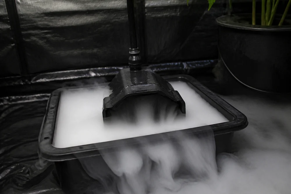 An ultrasonic fogger unit running in a reservoir inside a grow tent with dense white fog rolling out low across the floor