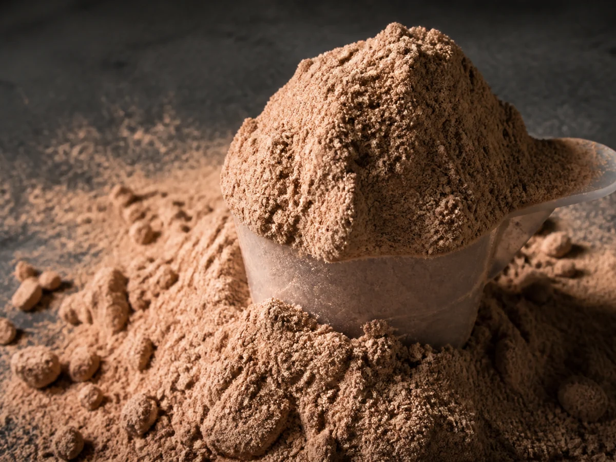 Measuring scoop heaped far above its rim with mushroom powder spilling onto a dark counter