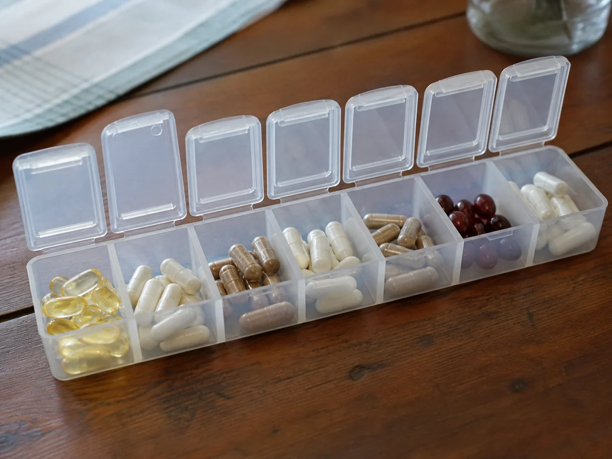 Open seven day pill organizer on a wooden table with different numbers of capsules in each compartment