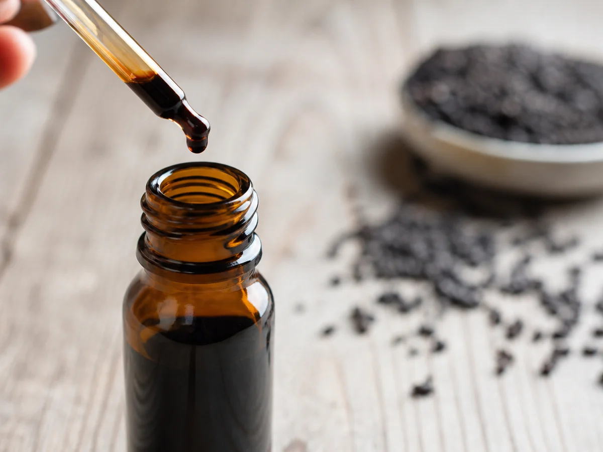 Amber dropper bottle of dark mushroom tincture with a single drop about to fall from the glass dropper
