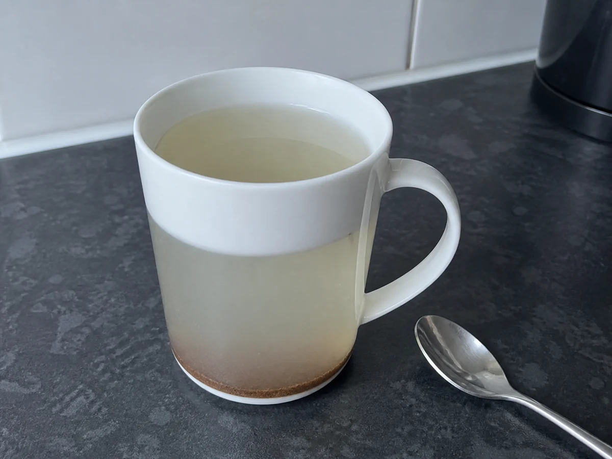 Plain white mug of pale watery mushroom tea with undissolved powder settled at the bottom