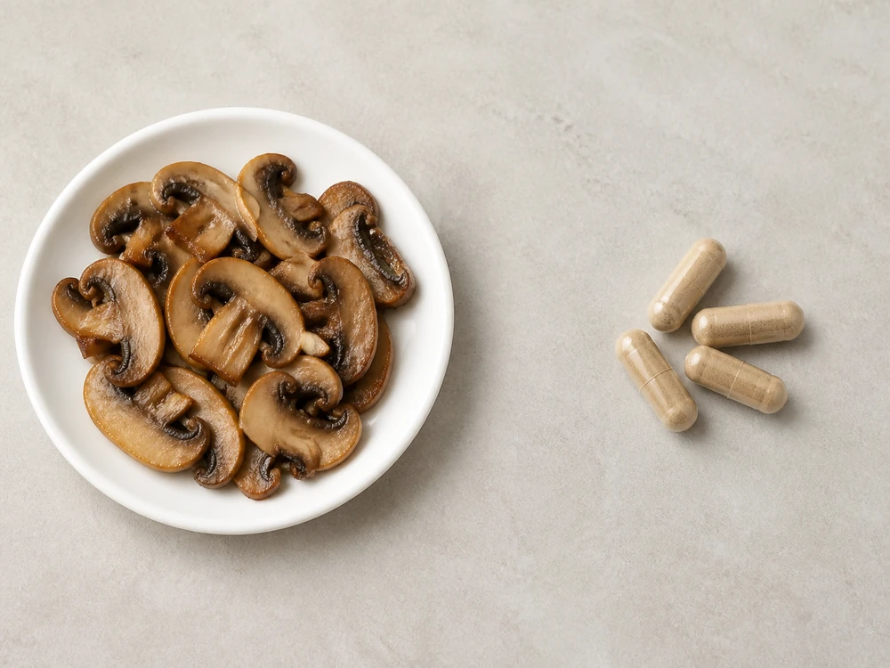 A cooked portion of mushroom on a plate beside a day's worth of extract capsules on a pale surface