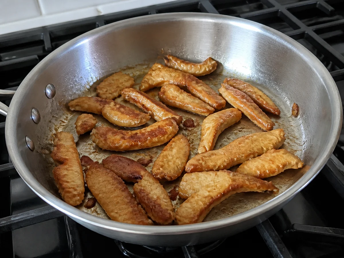 Strips of chicken of the woods cooked golden brown in a stainless steel pan