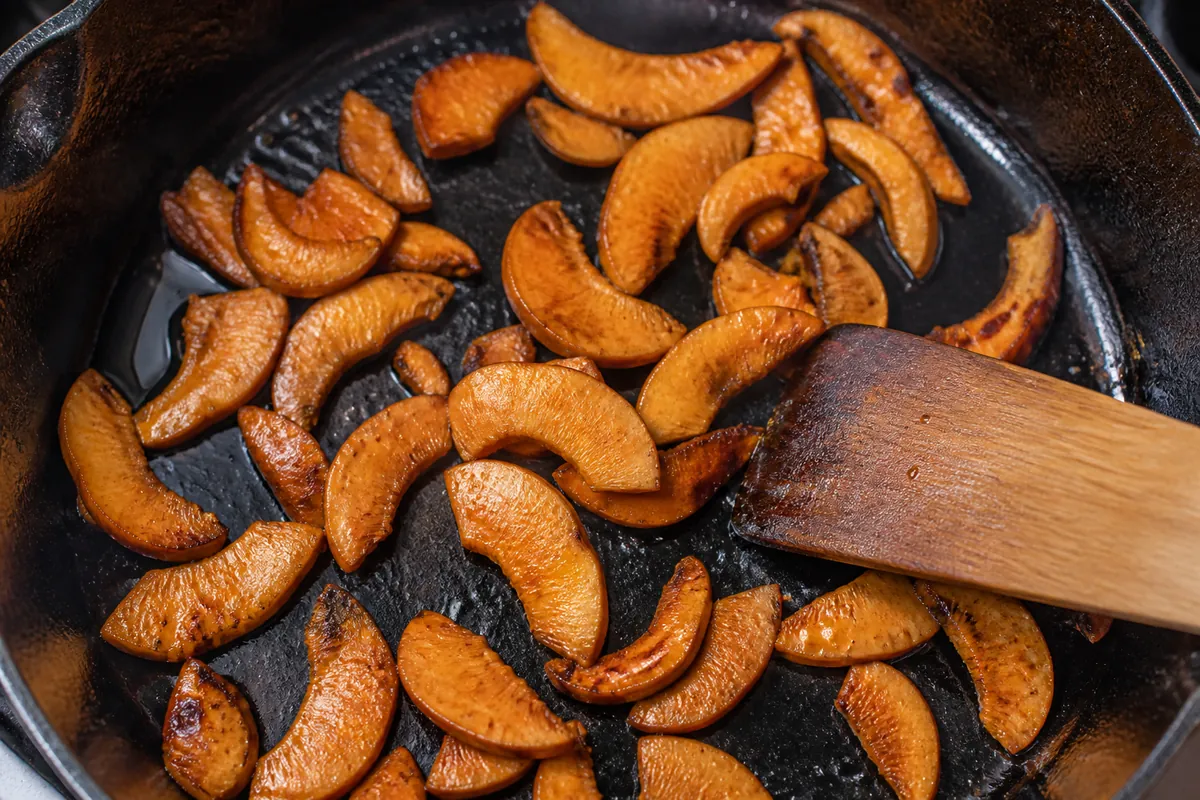 Orange saffron milk cap slices browning in a hot cast iron pan with edges crisping and holding their shape, turned with a wooden spatula