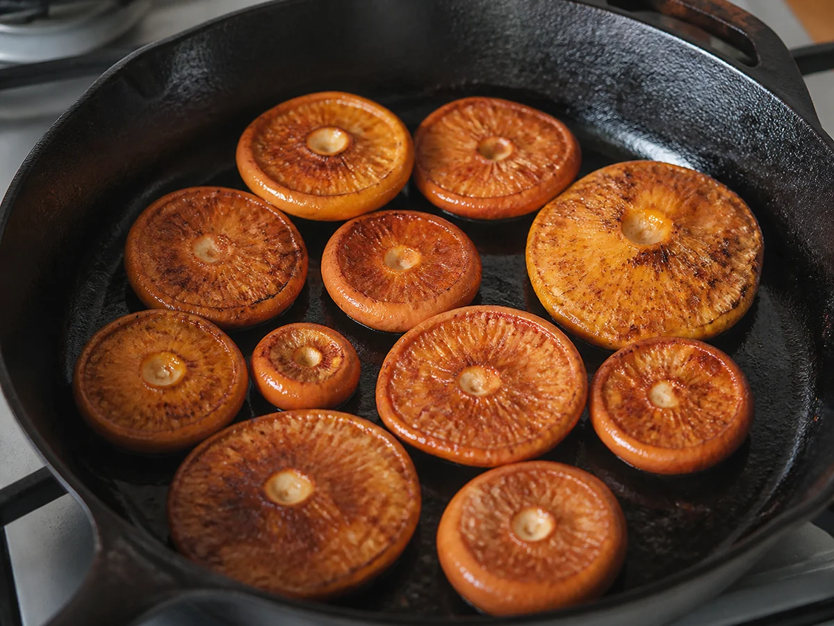 Halved orange saffron milk caps searing cut-side down in a hot cast iron pan with browned cut faces