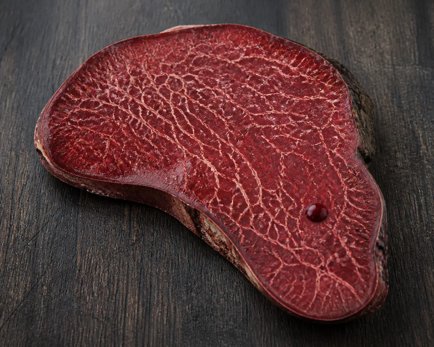 A beefsteak bracket cut through on a dark board showing deep red flesh marbled with pale veins and a bead of red juice