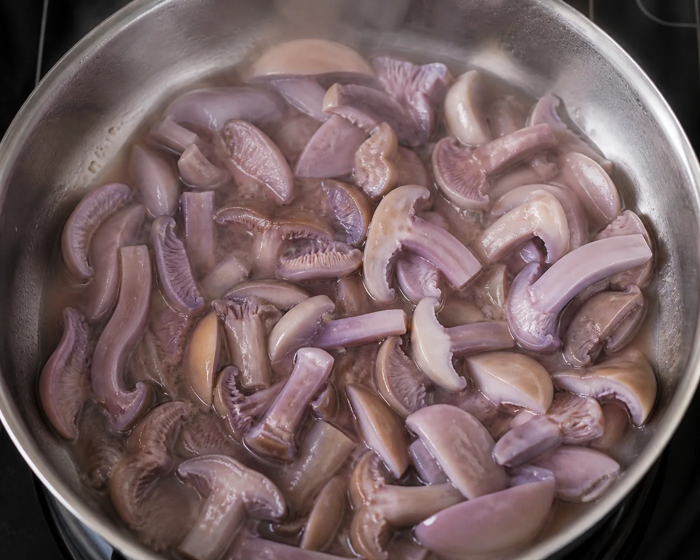 Sliced blewits sitting slack and pale in a shallow pool of their own liquid in a wet pan on a low heat