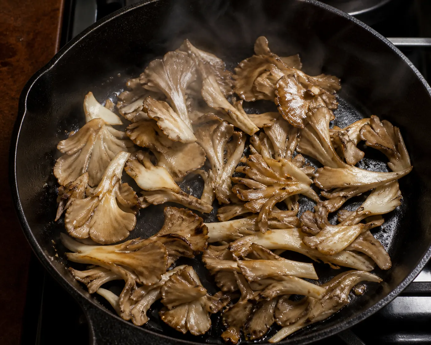 Torn maitake pieces in a hot skillet giving off steam with the edges beginning to brown