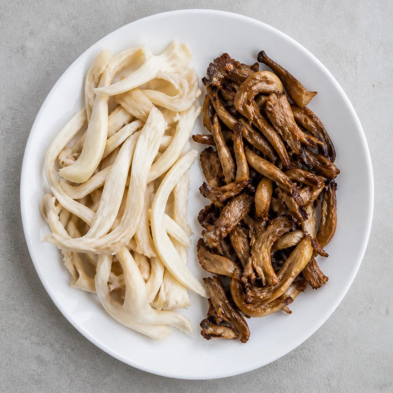 A plain plate split between pale limp raw oyster strips and deeply browned cooked ones
