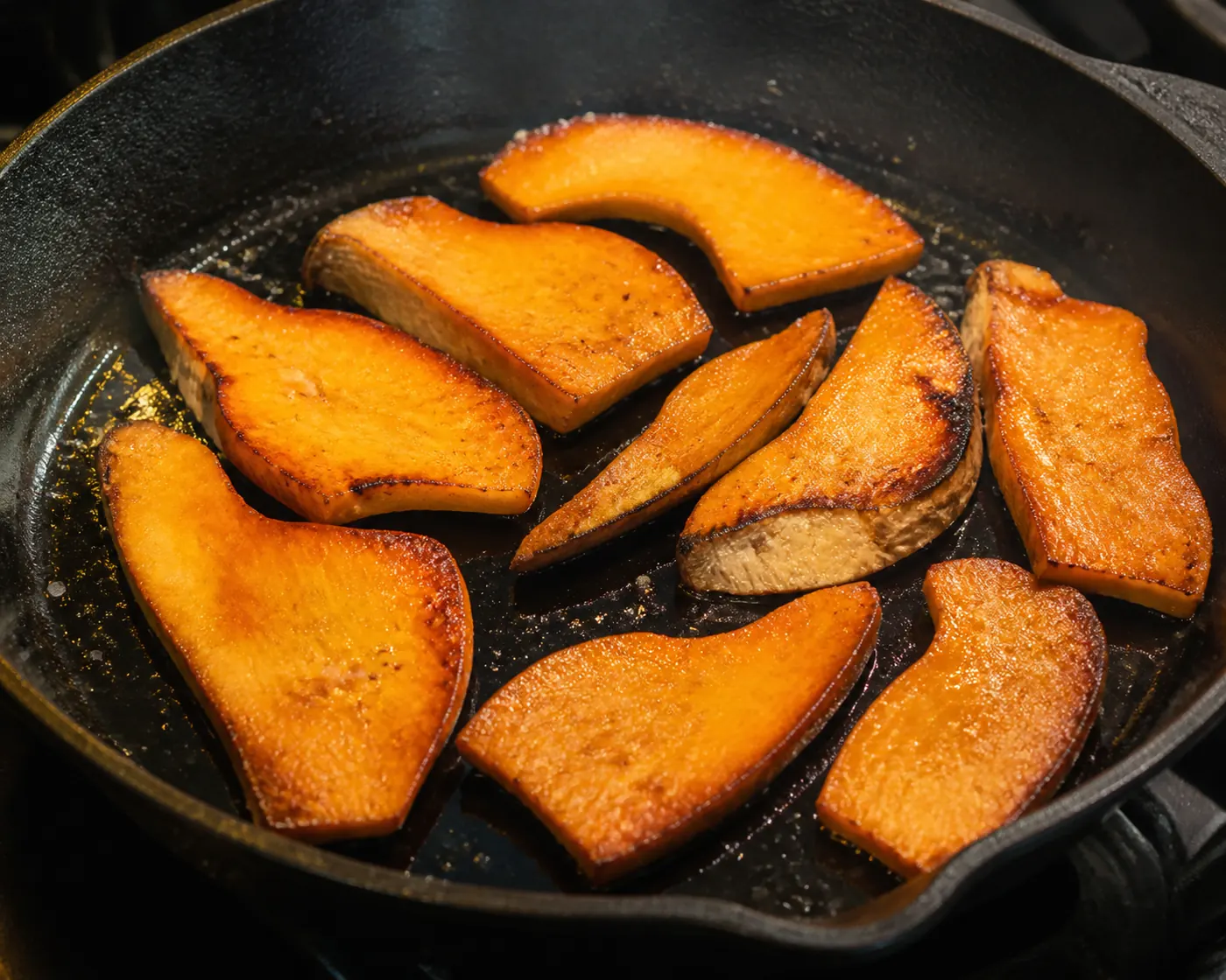 Thick orange mushroom slices browning in a hot cast iron pan with deeply caramelized edges and a little oil