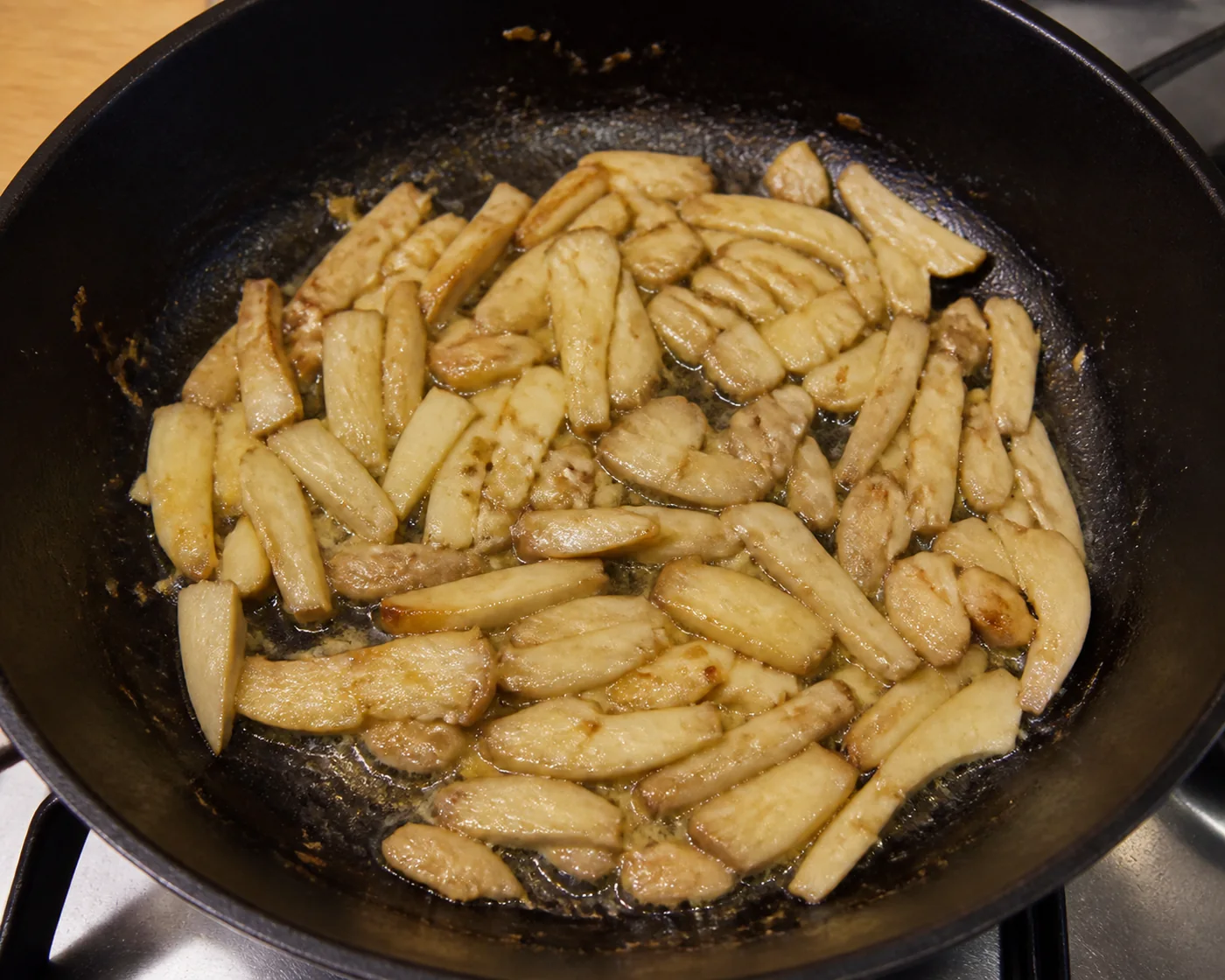 Sliced shaggy manes cooking down in a black skillet, greatly reduced and glossy pale gold with liquid released into the pan