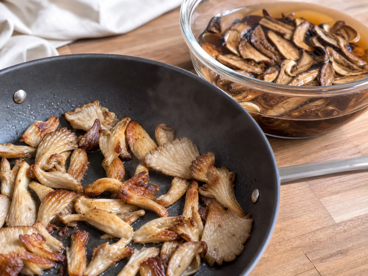 Browned oyster mushroom folds in a pan beside a bowl of soaking mushroom slices