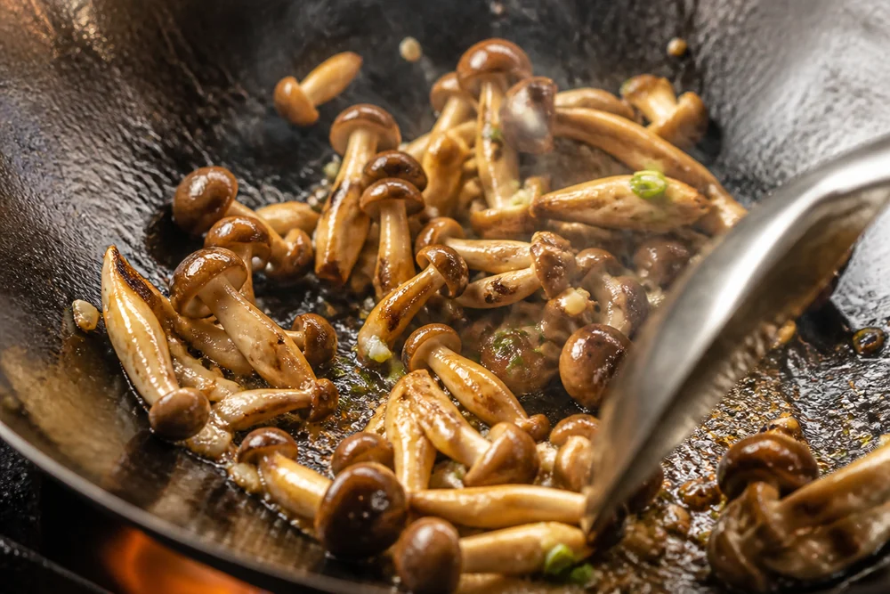 Small cluster mushrooms stir-frying over high heat in a wok, the pieces separate and browning rather than matted together