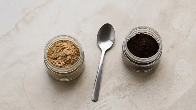 Open jar of coarse dried mushroom powder beside an open jar of fine dark extract powder with a spoon between them